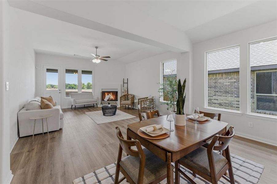 Open-concept living and dining area featuring wood-finish flooring, a white brick fireplace, and multiple large windows