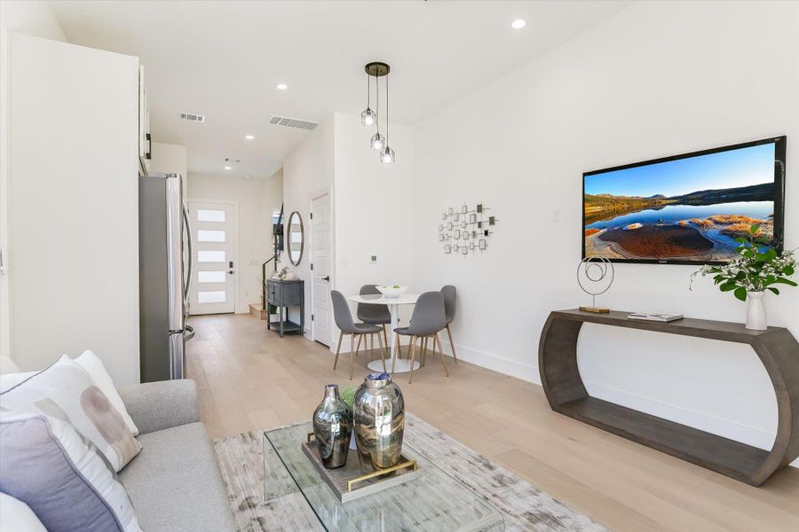 The light oak floors and high ceilings create an airy, expansive feel that connects the kitchen, dining, and outdoor spaces.