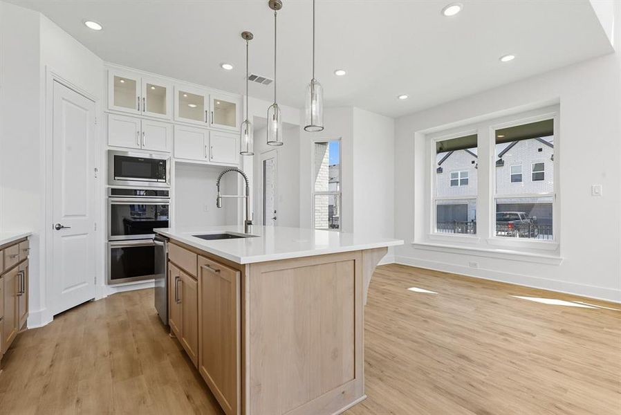 Kitchen with glass insert cabinets, pendant lighting, light wood-style floors, an island with sink, and recessed lighting Kitchen with glass insert cabinets, pendant lighting, light wood-style floors, an island with sink, and recessed lighting