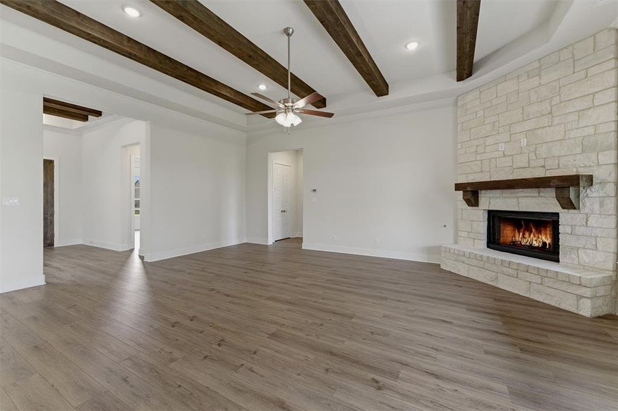 Spacious room featuring wood-finish flooring, a stone-clad corner fireplace with an integrated hearth, and a substantial wood mantel