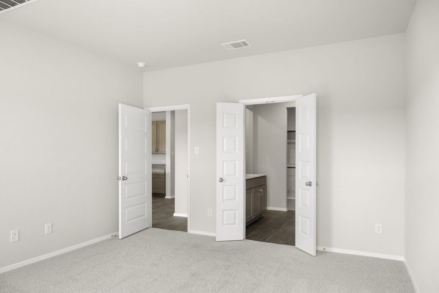 Image of home primary suite with door to main areas and one door to bathroom. Light carpet and white walls and doors