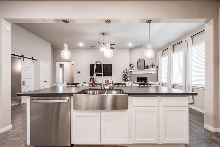 This home features a modern, open-concept kitchen with a large island, stainless steel sink, and sleek pendant lighting. It seamlessly flows into a cozy living area with a fireplace, perfect for entertaining. Natural light fills the space through large windows. This home features a modern, open-concept kitchen with a large island, stainless steel sink, and sleek pendant lighting. It seamlessly flows into a cozy living area with a fireplace, perfect for entertaining. Natural light fills the space through large windows.