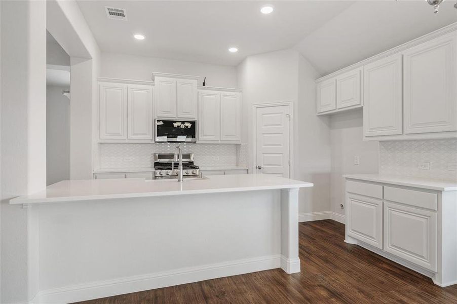 Kitchen featuring white cabinets, decorative backsplash, appliances with stainless steel finishes, dark wood finished floors, and recessed lighting
