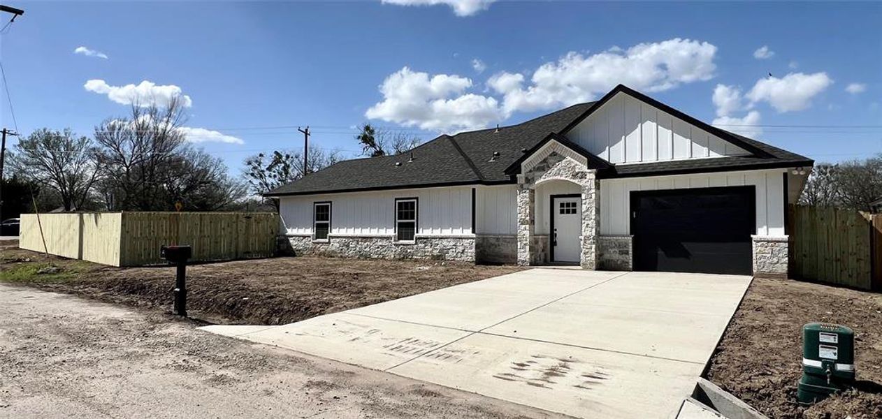 View of front of home with stone siding, fence, board and batten siding, concrete driveway, and an attached garage