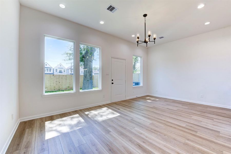 Living area framed by large windows that bring in natural light, paired with wood-look LVP flooring and tall ceilings. Statement chandelier adds a refined focal point, while direct access to the backyard enhances everyday flow.