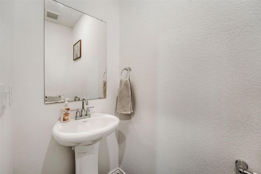 Downstairs half bathroom White pedestal sink with chrome faucet, large frameless mirror, and neutral-toned wall finish Downstairs half bathroom White pedestal sink with chrome faucet, large frameless mirror, and neutral-toned wall finish