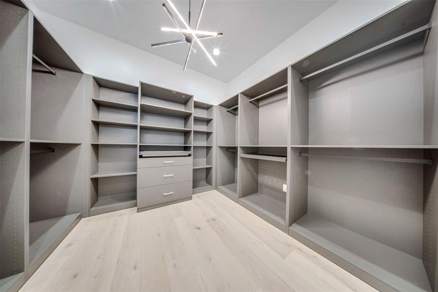 Spacious closet featuring light hardwood / wood-style flooring and an inviting chandelier