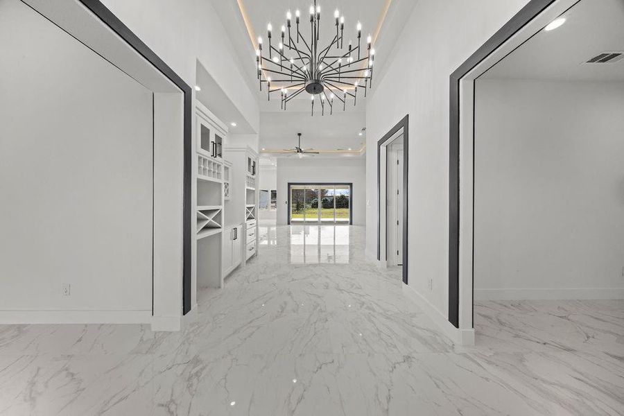 Hallway with light marble finish flooring, a chandelier, and a high ceiling