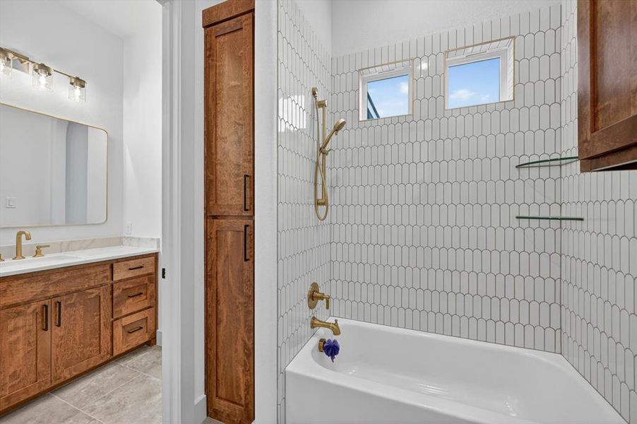 Bathtub with stylized tile surround, dual windows, and brass fixtures