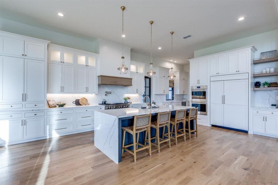 Kitchen featuring backsplash, light wood-style flooring, a breakfast bar area, an island with sink, and white cabinets Kitchen featuring backsplash, light wood-style flooring, a breakfast bar area, an island with sink, and white cabinets