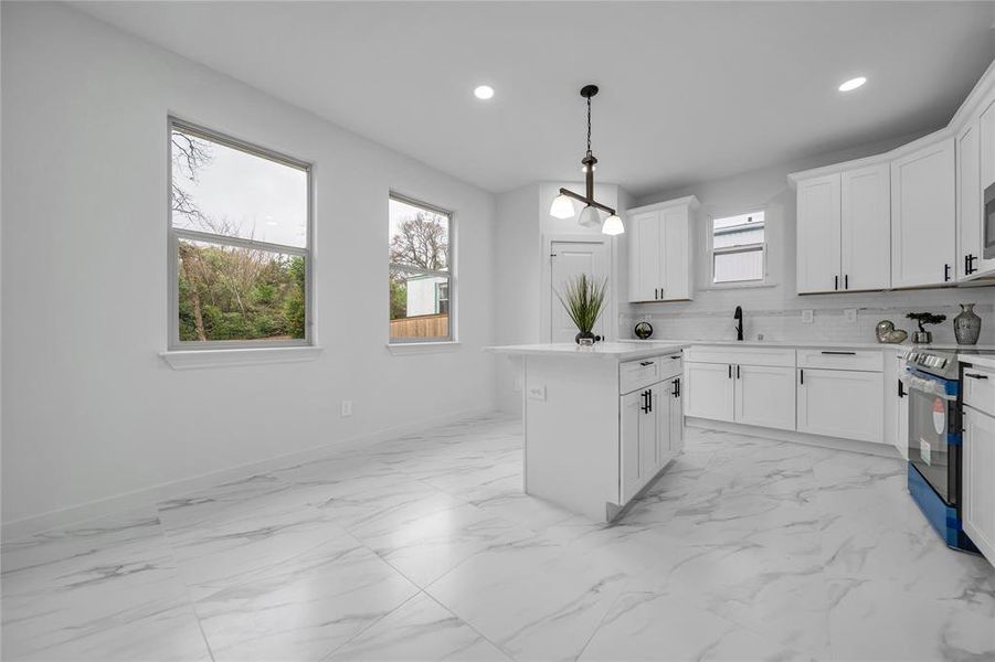 Kitchen with decorative light fixtures, white cabinets, decorative backsplash, stainless steel range with electric stovetop, and a center island