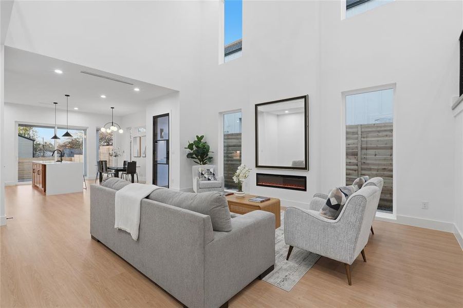 Living room with light wood-style flooring, healthy amount of natural light, hanging lights, and a high ceiling