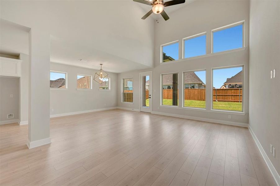 Spacious room featuring soaring ceilings, a ceiling fan, and light wood-finish flooring