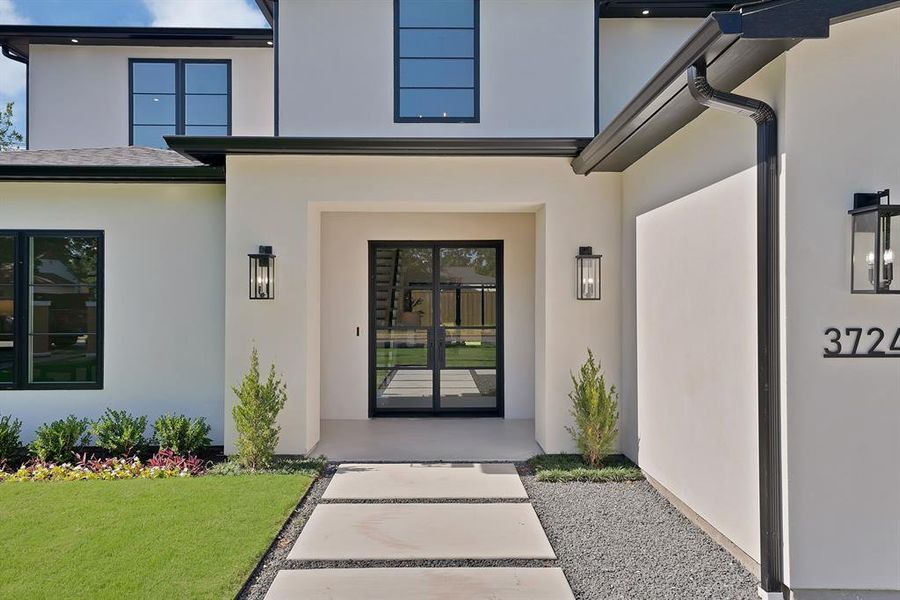Modern stucco facade with black-framed windows and a double glass entry door