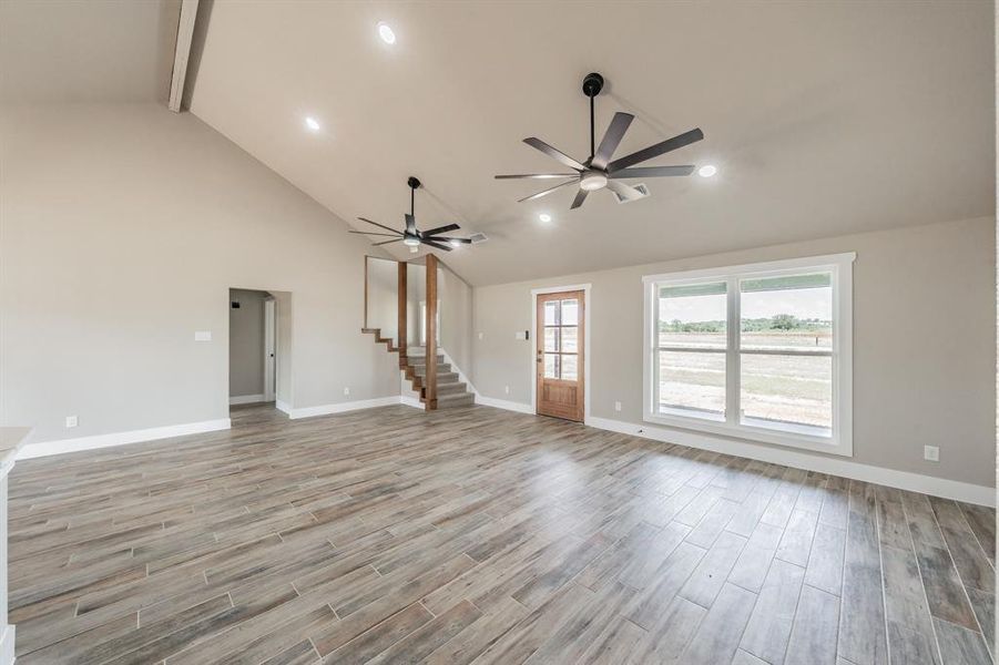 Unfurnished living room with beamed ceiling, light wood-style floors, high vaulted ceiling, stairway, and recessed lighting Unfurnished living room with beamed ceiling, light wood-style floors, high vaulted ceiling, stairway, and recessed lighting