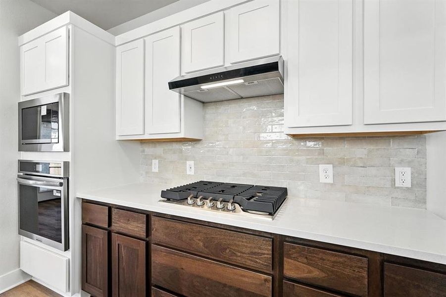 Kitchen featuring backsplash, appliances with stainless steel finishes, white cabinets, under cabinet range hood, and light stone counters Kitchen featuring backsplash, appliances with stainless steel finishes, white cabinets, under cabinet range hood, and light stone counters