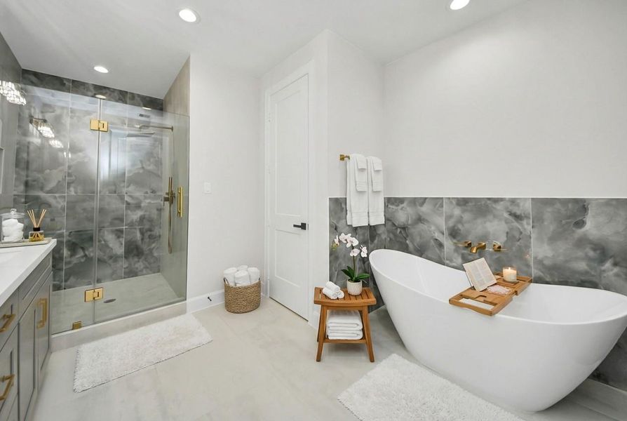 Spa-inspired primary bathroom featuring a freestanding soaking tub, oversized glass-enclosed shower, designer tile accents, and elegant gold fixtures for a true retreat experience.