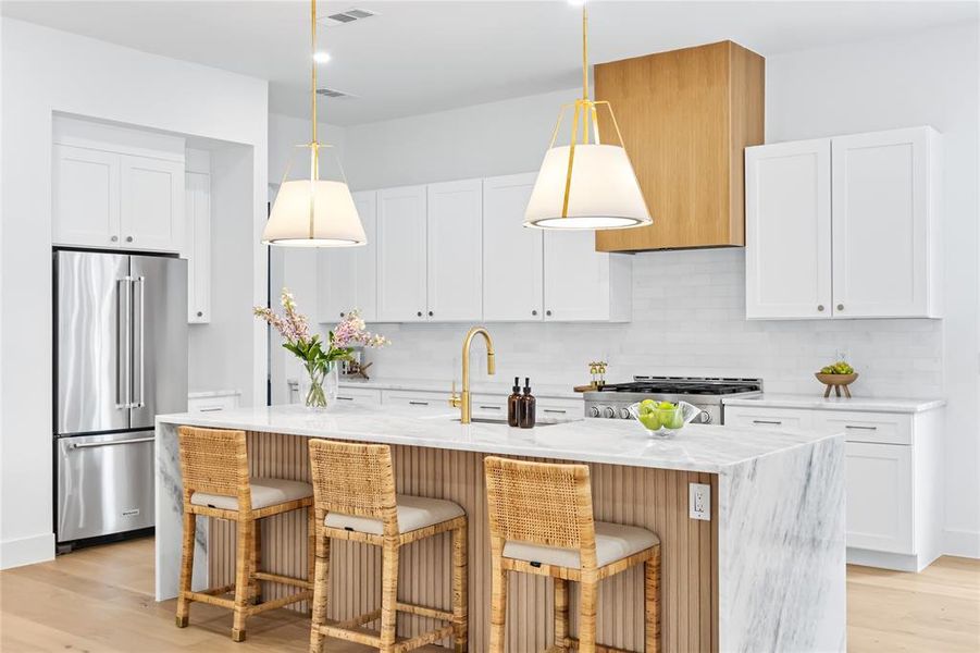 Kitchen with an island with sink, high quality fridge, white cabinets, and decorative light fixtures