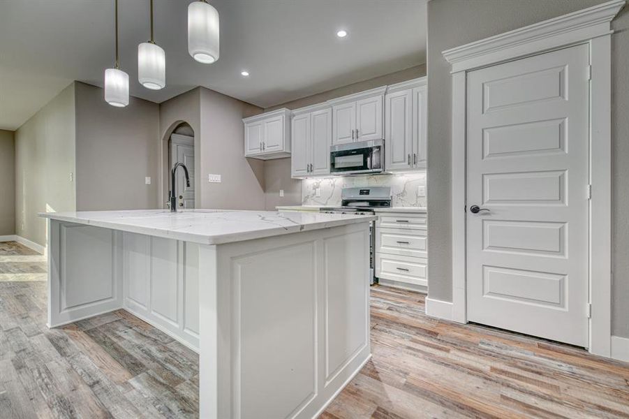Kitchen featuring white cabinetry, light stone countertops, hanging light fixtures, tasteful backsplash, and stainless steel appliances