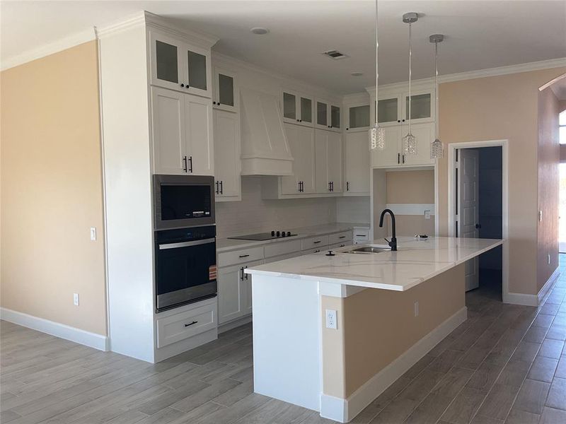 Kitchen featuring ornamental molding, premium range hood, light stone counters, hanging light fixtures, and light wood-style floors Kitchen featuring ornamental molding, premium range hood, light stone counters, hanging light fixtures, and light wood-style floors