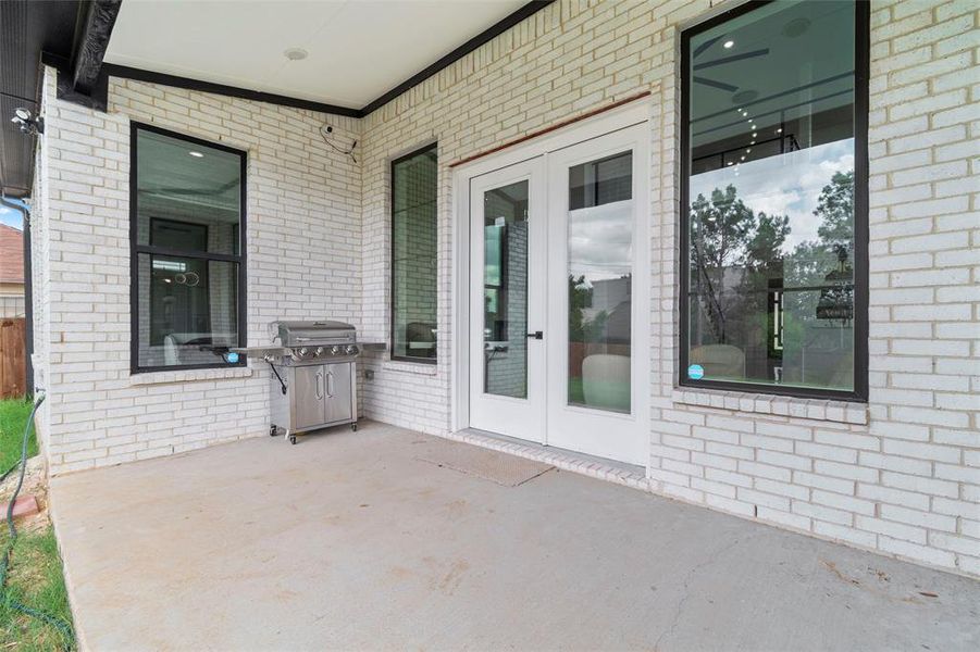 Covered patio featuring white painted brick exterior, concrete flooring, and multiple large windows with black frames