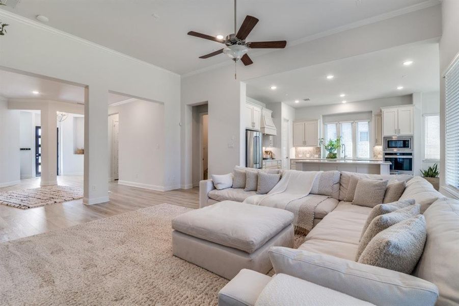Living room featuring light wood-type flooring, baseboards, recessed lighting, a ceiling fan, and ornamental molding Living room featuring light wood-type flooring, baseboards, recessed lighting, a ceiling fan, and ornamental molding