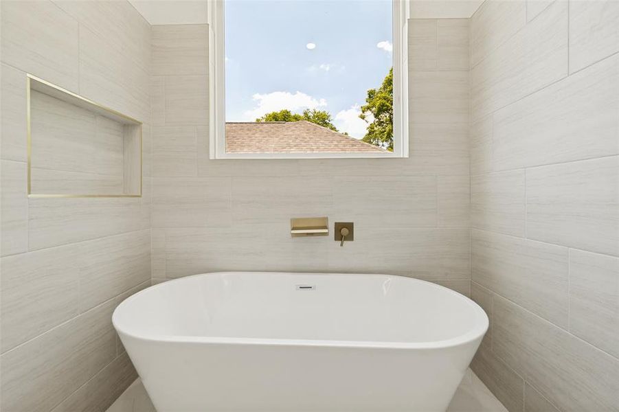 Freestanding soaking tub with wall-mounted brass fixtures, set against light-toned tiled walls Freestanding soaking tub with wall-mounted brass fixtures, set against light-toned tiled walls