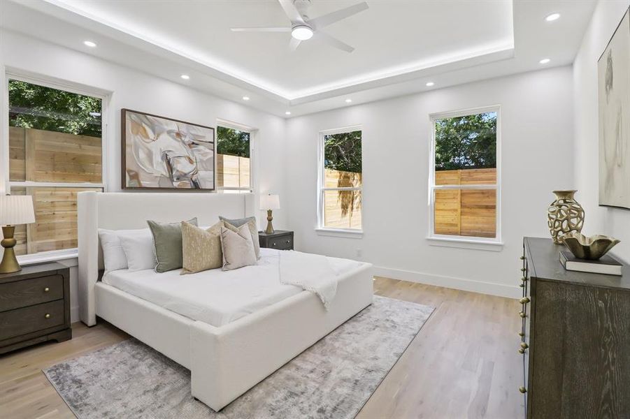 Bedroom featuring multiple windows, light wood-style flooring, recessed lighting, and a raised ceiling