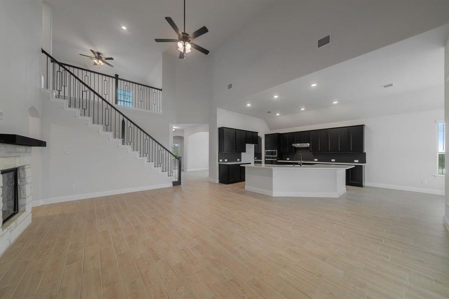 Kitchen with light wood-type flooring, ceiling fan, sink, an island with sink, and high vaulted ceiling