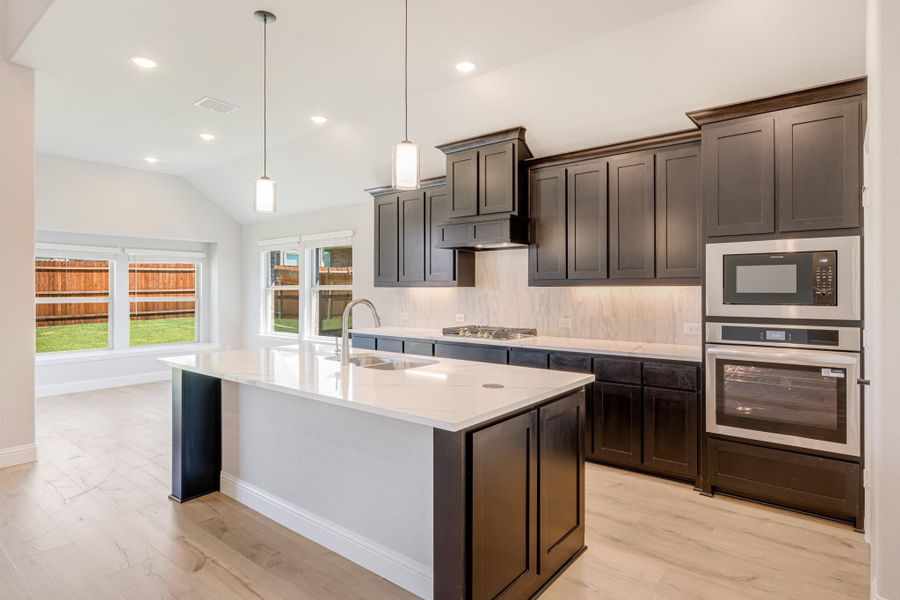 Kitchen with dark cabinets, white quartz island, stainless steel appliances, and light hardwood floors Kitchen with dark cabinets, white quartz island, stainless steel appliances, and light hardwood floors