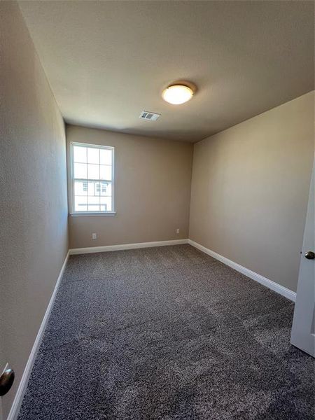 Spare room featuring visible vents, dark carpet, and baseboards