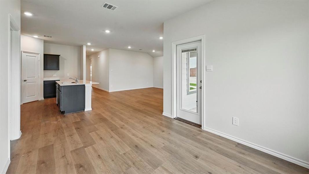 Kitchen featuring a center island with sink, recessed lighting, open floor plan, light wood finished floors, and dark cabinetry