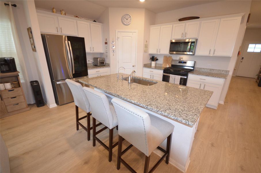 Kitchen with appliances with stainless steel finishes, light wood-type flooring, white cabinetry, a center island with sink, and a kitchen breakfast bar Kitchen with appliances with stainless steel finishes, light wood-type flooring, white cabinetry, a center island with sink, and a kitchen breakfast bar