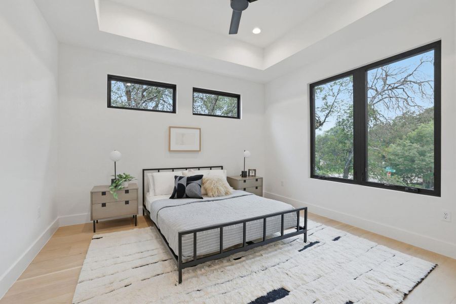 Bedroom featuring a tray ceiling with recessed lighting, light wood-finish flooring, and large windows with black framing