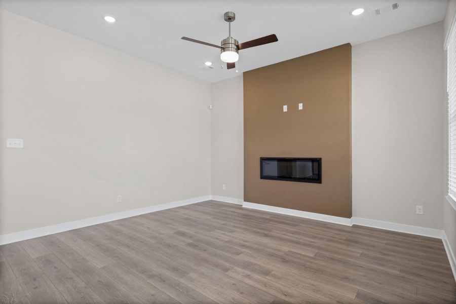 Recessed lighting, wood-finish flooring, a ceiling fan, and a built-in fireplace feature a distinct accent wall
