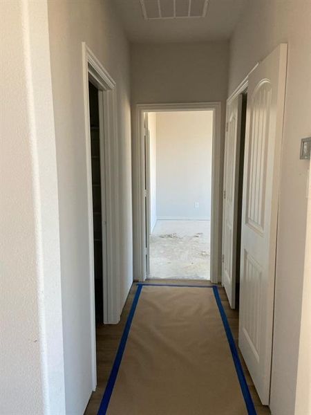 Hallway featuring white panel doors, neutral wall paint, and wood-finish flooring