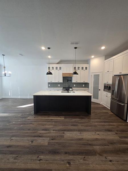 Kitchen with tasteful backsplash, white cabinetry, pendant lighting, appliances with stainless steel finishes, and a center island with sink