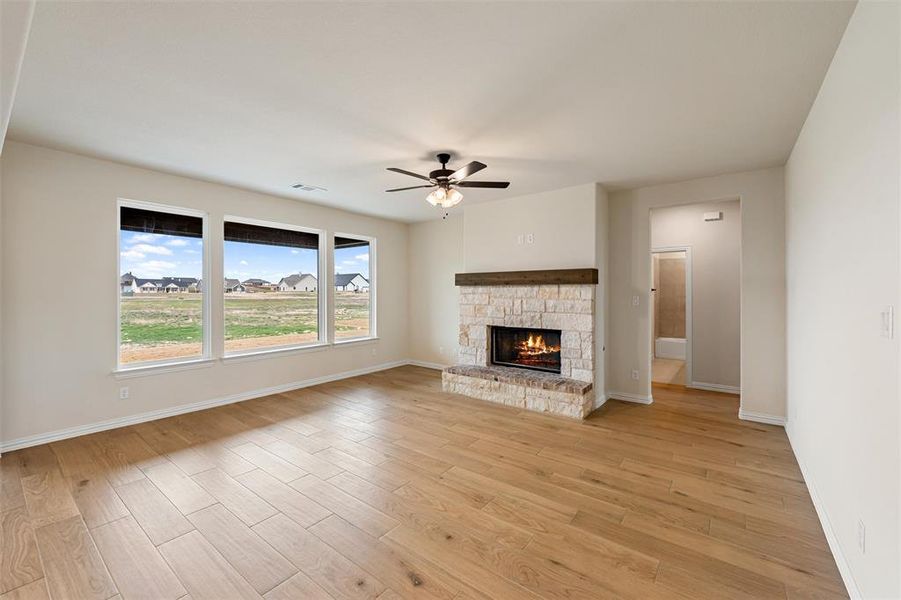 Unfurnished living room featuring light wood-style floors, a stone fireplace, and a ceiling fan