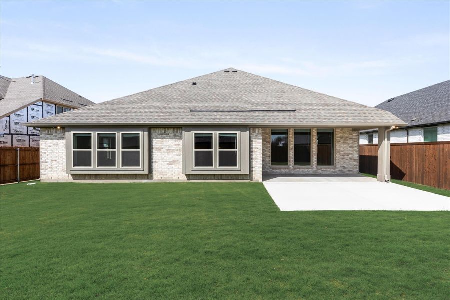 Rear exterior of single-story brick home with large windows, concrete patio, and fenced backyard lawn