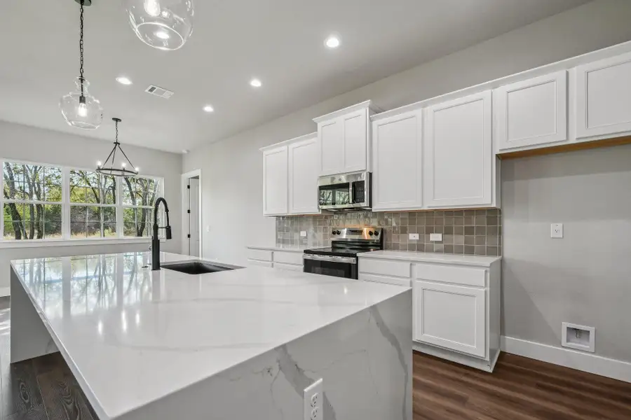 Kitchen with pendant lighting, appliances with stainless steel finishes, light stone countertops, white cabinetry, and decorative backsplash