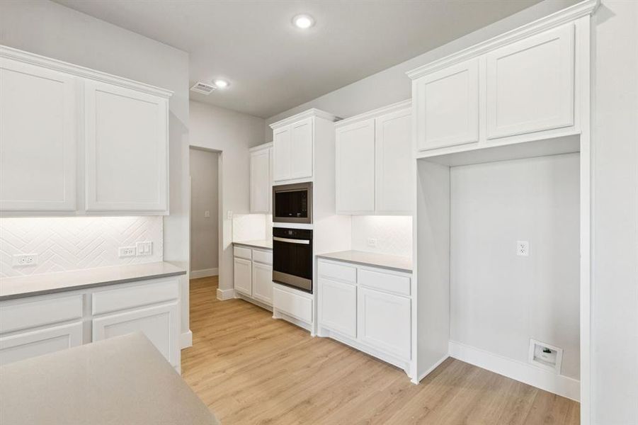 Kitchen featuring white cabinets, decorative backsplash, light wood finished floors, oven, and stainless steel microwave