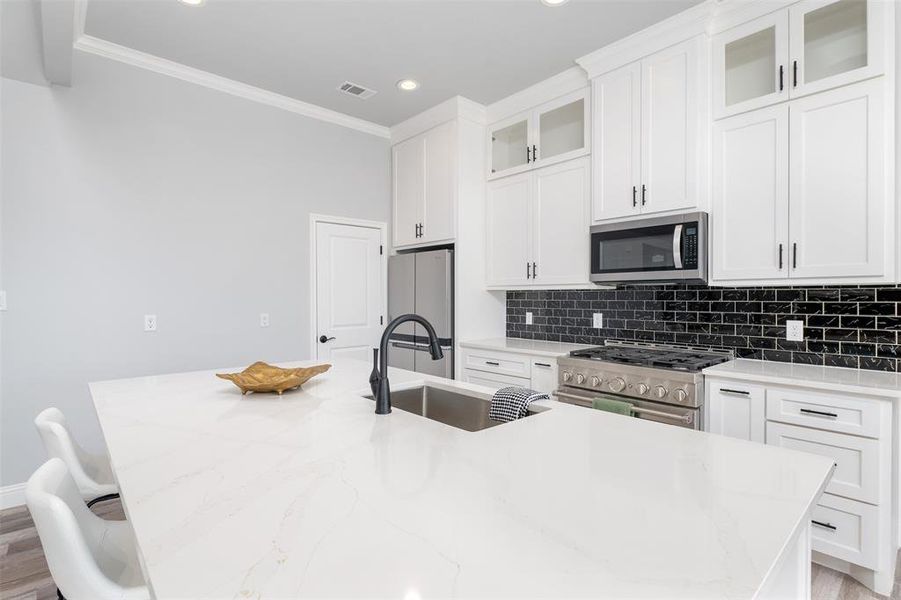 Kitchen with a breakfast bar, sink, white cabinetry, stainless steel appliances, and a kitchen island with sink