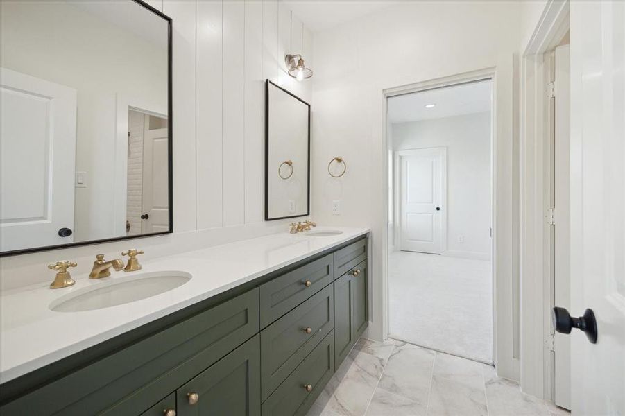 Sleek design and functionality define this Jack and Jill bathroom. Dual sinks with brass fixtures are set in a bold green vanity, offering plenty of storage and a striking contrast against the crisp white walls. Vertical shiplap adds subtle texture, while the marble-look tile flooring enhances the space with timeless elegance. Black-framed mirrors and warm gold accents tie the design together, creating a stylish yet practical bathroom perfect for shared use.