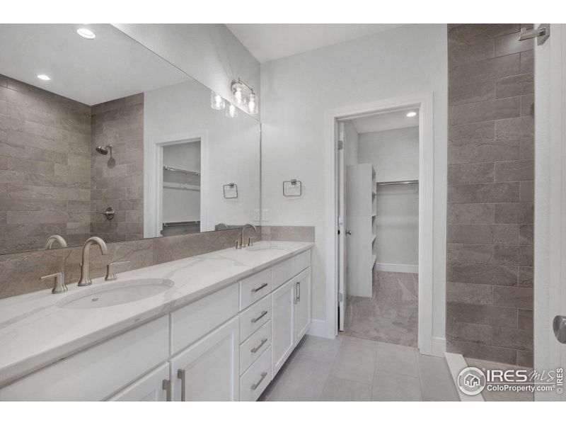 The primary ensuite, featuring dual vanities, a full-width mirror, porcelain tile flooring, and porcelain vanity sinks