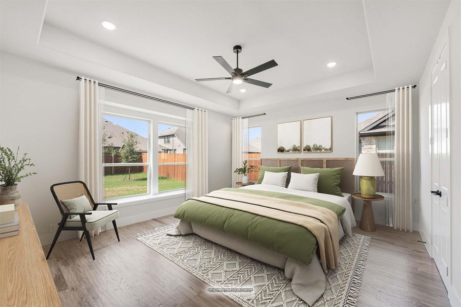 Bedroom with tray ceiling, ceiling fan, hardwood floors, and large windows with green bedding and natural light.