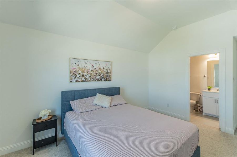 Bedroom featuring vaulted ceilings, light gray carpet, and an en-suite bathroom with a white vanity and tiled flooring