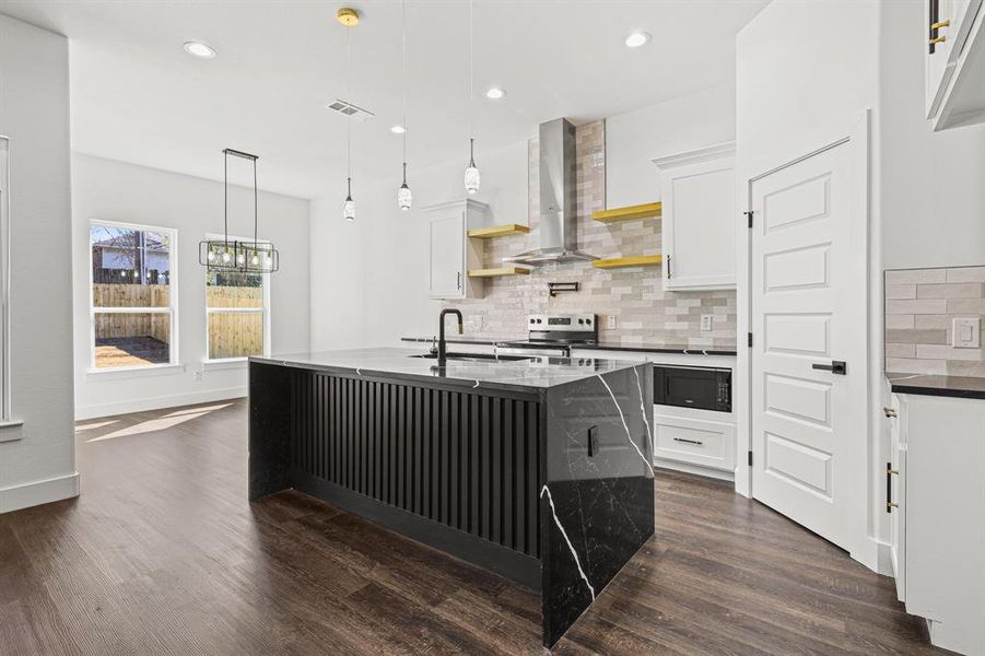 Kitchen with black microwave, open shelves, white cabinetry, wall chimney exhaust hood, and a center island with sink