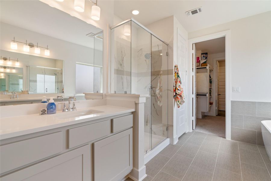 Dual vanities, a walk-in shower, and tile flooring grace the primary bathroom.