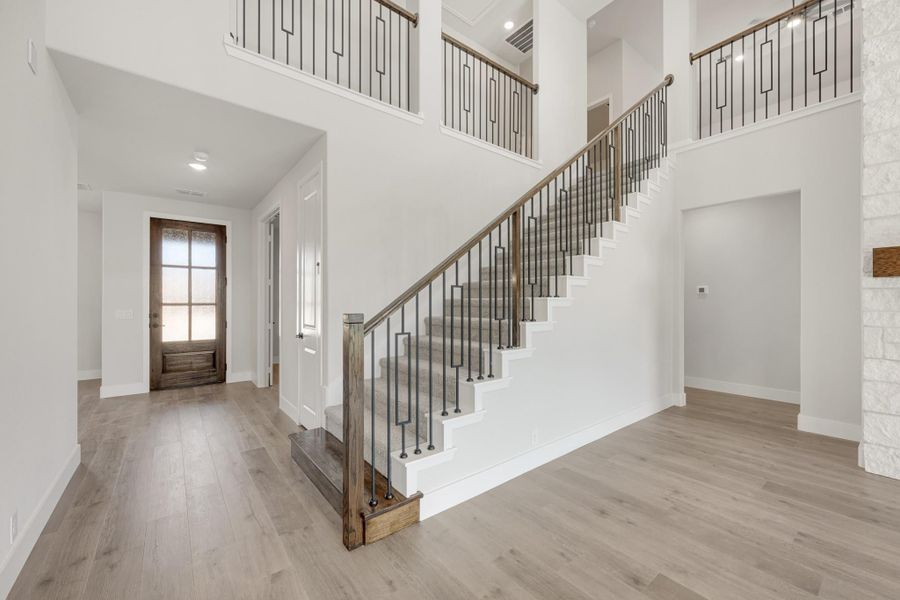 Two-story foyer with wood and iron staircase, light hardwood floors, and wood front door Two-story foyer with wood and iron staircase, light hardwood floors, and wood front door