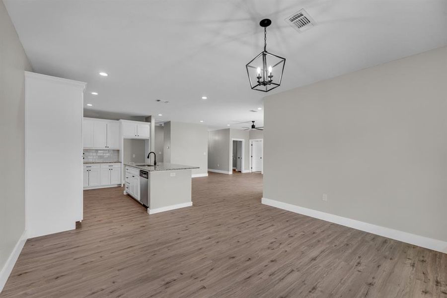 Unfurnished living room with ceiling fan with notable chandelier, sink, and light hardwood / wood-style floors